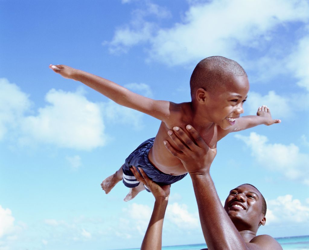 Father lifting son (6-8 years) in air at beach, son pretending to fly