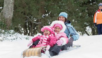 Mother and daughters sledding on snowy hill outdoors