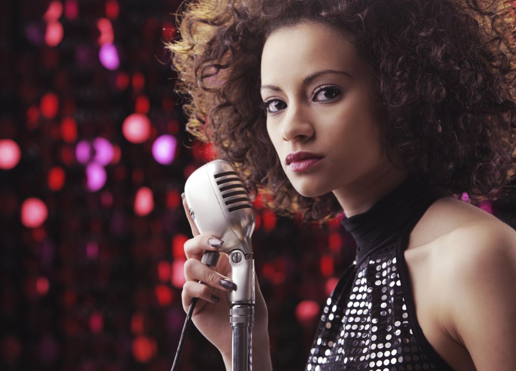 Young female singer with brown curly hair singing a song