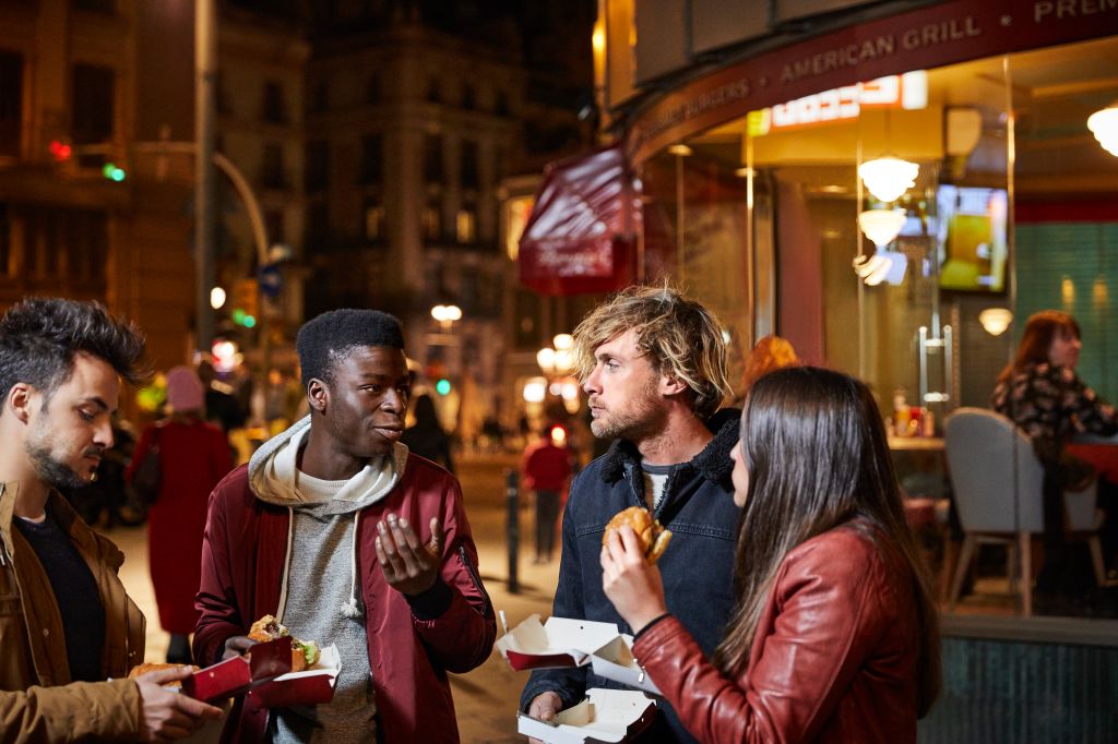 Man talking to friends while having burger in city