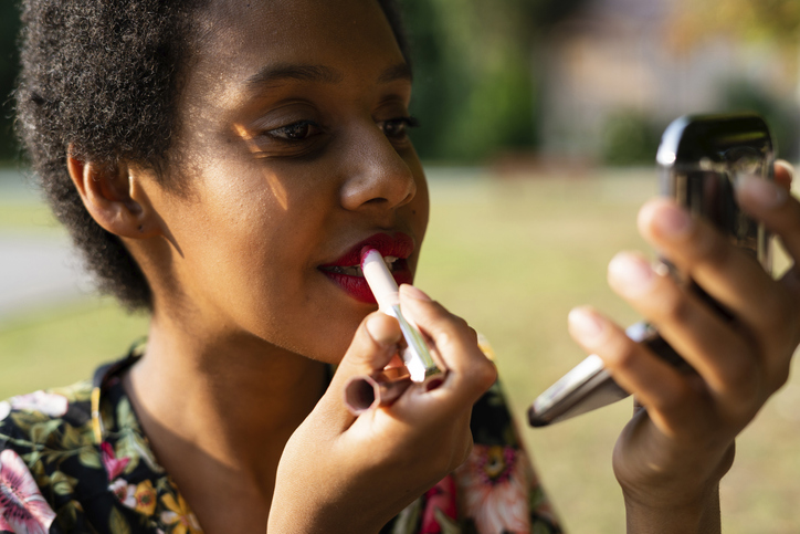 Portrait of young woman applying lipstick outdoors