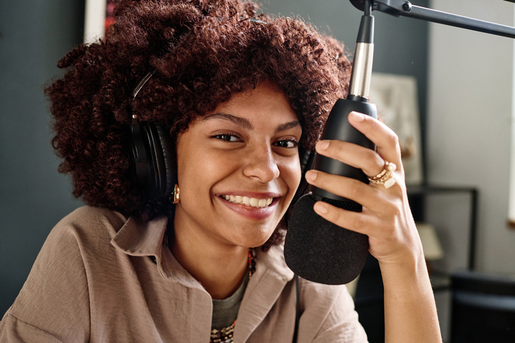 Young cheerful woman holding microphone and looking at camera