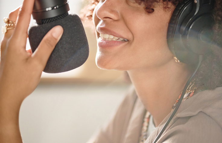 Close-up of young smiling woman in headphones touching microphone