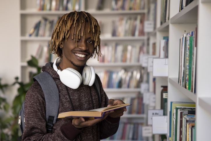 African student guy pose with book in hands in library